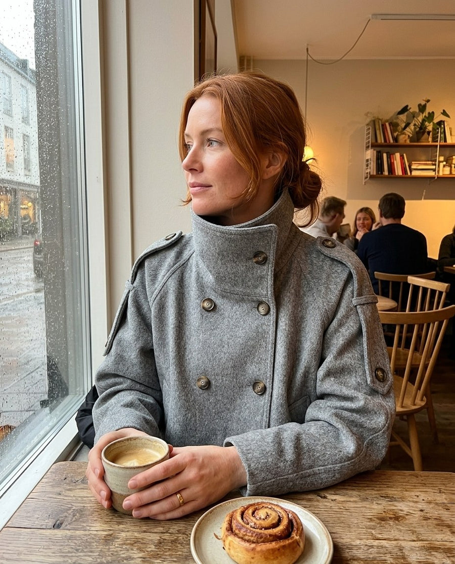 Grå dubbelknäppt jacka på ett kafé med kaffe och kanelbulle