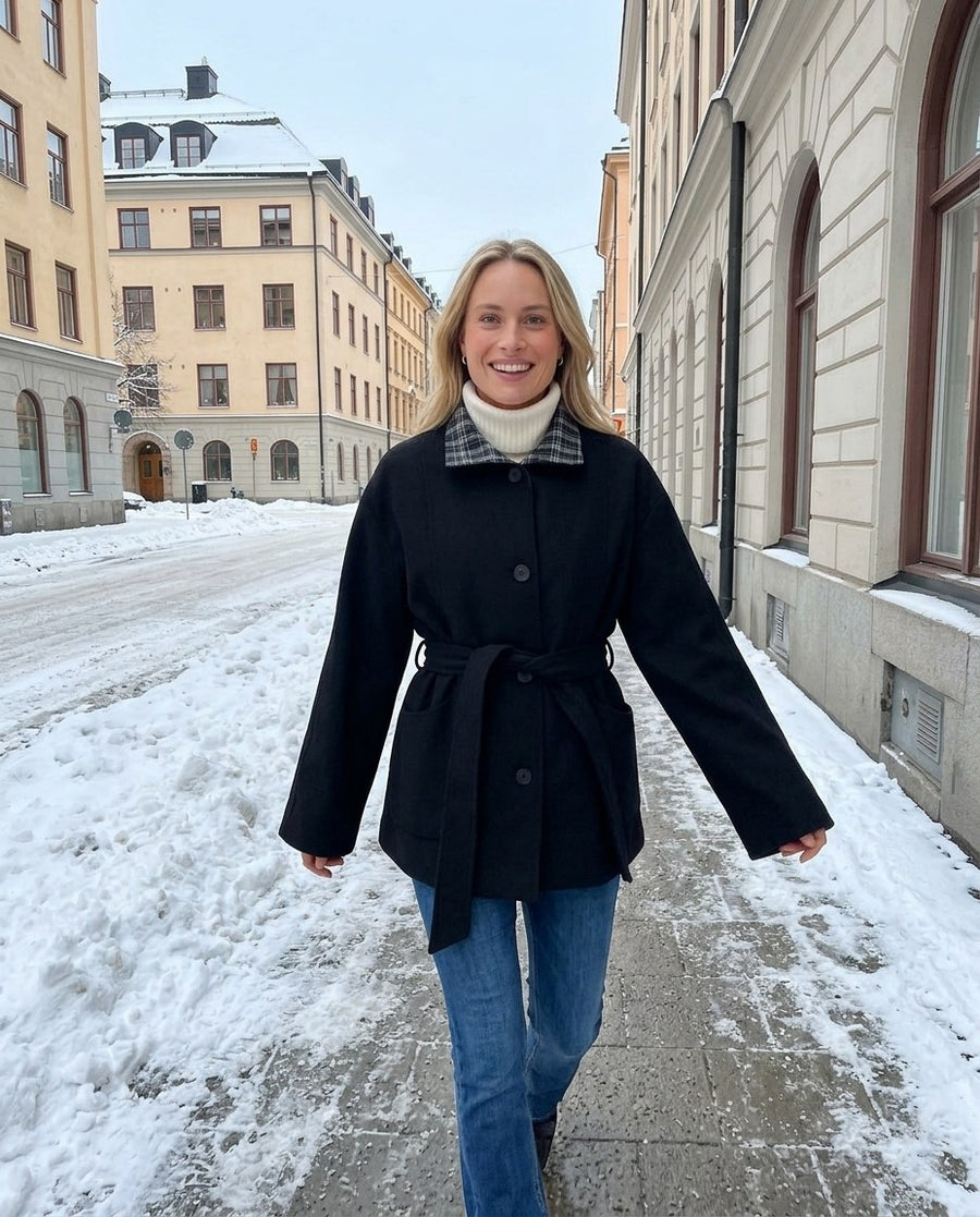 Greta, kappa med skärp och kontrastkrage för dam i svart, stylinginspiration på en snöig gata