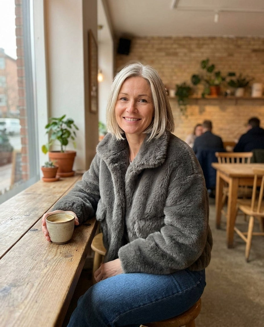 Hedda, kort jacka i mjuk fuskpäls för dam i grå, stylinginspiration på ett kafé