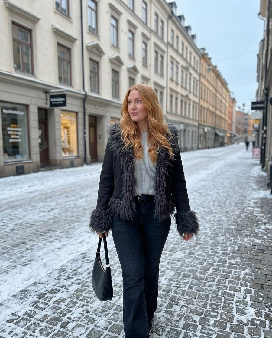 Selma, kort jacka med fuskpälskant för dam i svart, stylinginspiration på en snöig gata