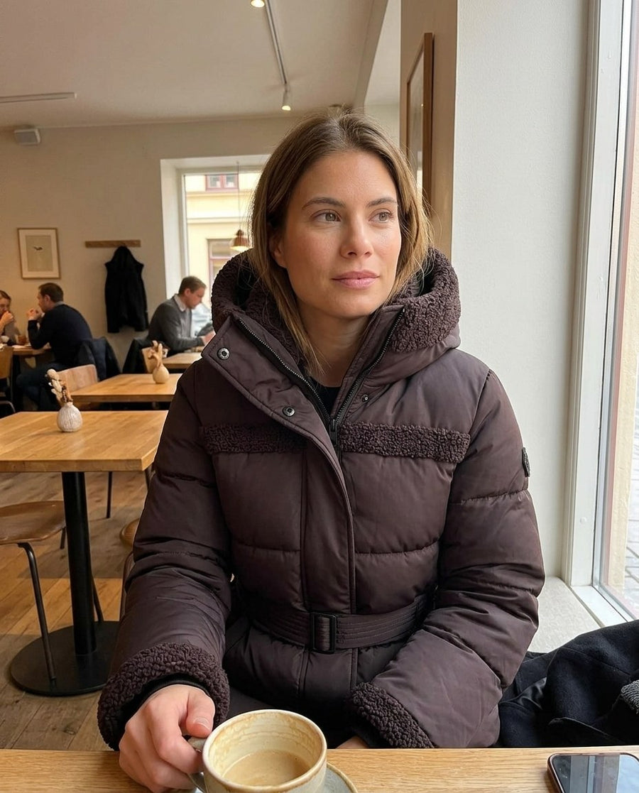 Signe, vadderad 2-i-1-jacka med huva för dam i mörkbrun, stylinginspiration på ett kafé
