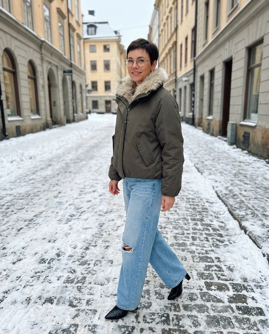 Svea, vadderad bomberjacka med hög krage för dam i mörk olivgrön, stylinginspiration på en snöig gata