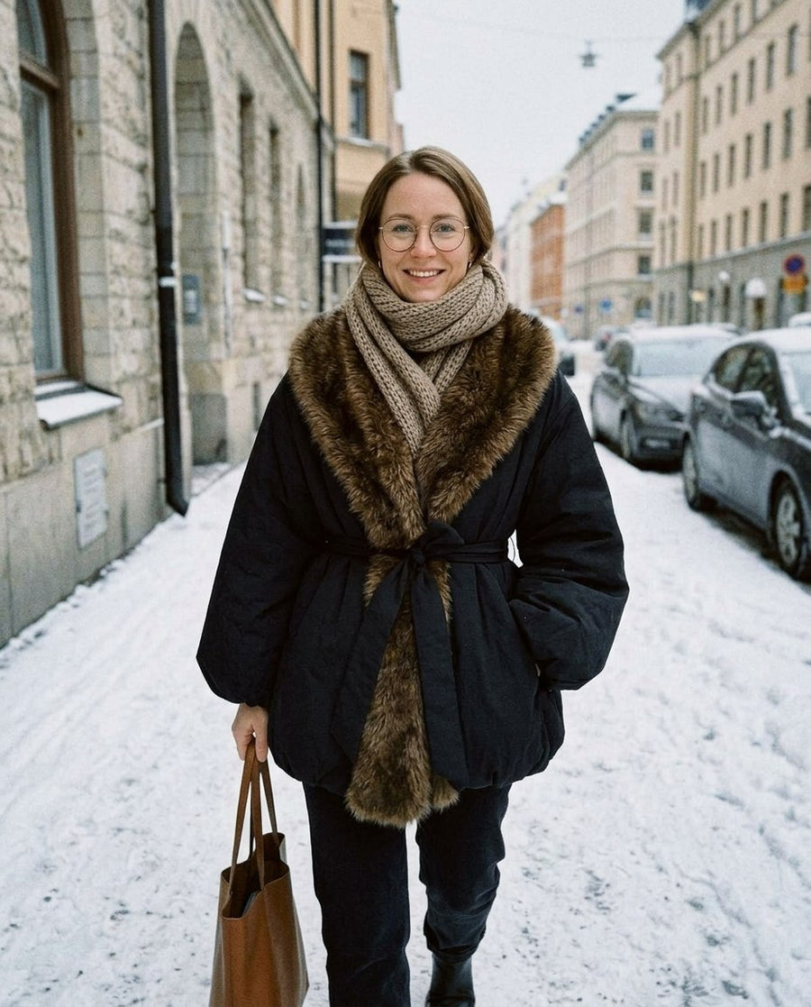 Tilda, vadderad damjacka med fuskpälskrage och skärp i svart, stylinginspiration på en snöig gata